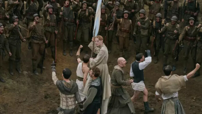 Coward 02 (1) A pale-robed man at the center holds a blue flag as soldiers close in with weapons around him in a chaotic battle on a muddy ground.