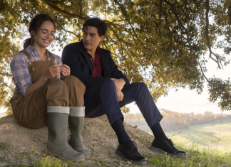 Romance APAIXONANTE ambientado em vinícolas italianas vira fenômeno no Prime Video; Conheça! Two people sit on a grassy hillside beneath a tree, chatting as the woman in brown overalls shows something to the man in a dark suit and red shirt.