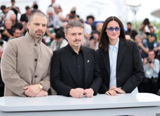 Entrevista | “A arte não precisa resolver problemas”: Sebastian Stan e Mungiu debatem polarização política em ‘Fjord’ (Cannes 2026) Three formally dressed individuals pose behind a white table at a press event, with photographers in the background.