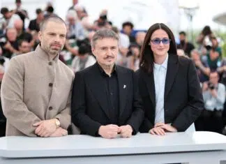 Entrevista | “A arte não precisa resolver problemas”: Sebastian Stan e Mungiu debatem polarização política em ‘Fjord’ (Cannes 2026) Three formally dressed individuals pose behind a white table at a press event, with photographers in the background.