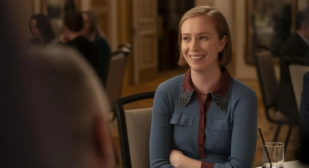 Hannah-Einbinder-mediocres (1) Smiling woman in a blue cardigan sits at a dining table during a social event.