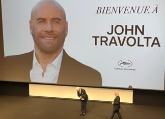 John Travolta é surpreendido com Palma de Ouro Honorária em Cannes: “Isso é maior que o Oscar” Large screen showing a portrait of John Travolta with the words 'BIENVENUE À JOHN TRAVOLTA' and a Cannes Festival logo; two men on stage in front of it.