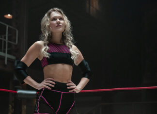 ‘Prison Break’: Atriz de ‘Heels’ se junta ao elenco do reboot Athlete in a wrestling ring poses with hands on hips, wearing a pink-and-black sports bra and shorts and elbow guards.