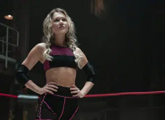 ‘Prison Break’: Atriz de ‘Heels’ se junta ao elenco do reboot Athlete in a wrestling ring poses with hands on hips, wearing a pink-and-black sports bra and shorts and elbow guards.