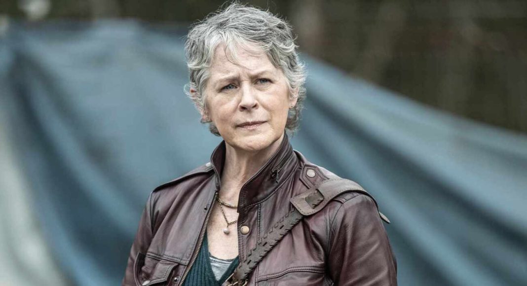 Woman with short gray hair in a brown leather jacket, standing outdoors with a blue tent in the background.