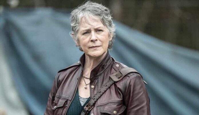 Woman with short gray hair in a brown leather jacket, standing outdoors with a blue tent in the background.