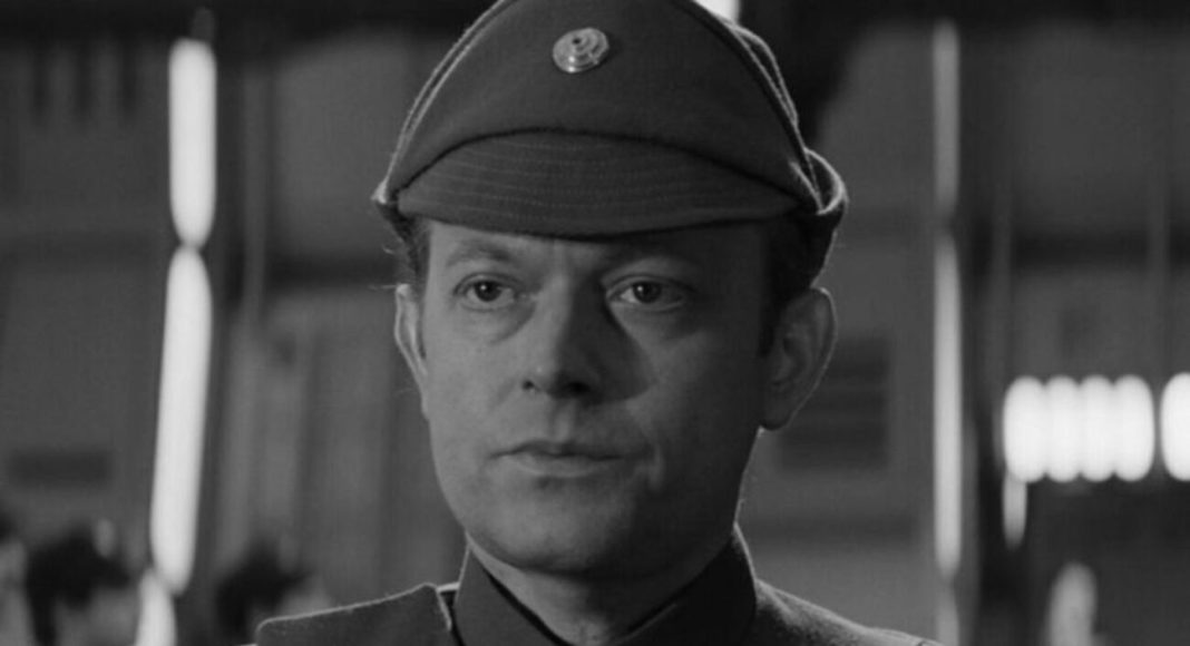 Black-and-white portrait of a man in a vintage military uniform and cap, looking slightly to the left in a blurred indoor setting.