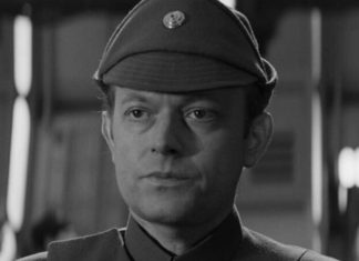 Black-and-white portrait of a man in a vintage military uniform and cap, looking slightly to the left in a blurred indoor setting.