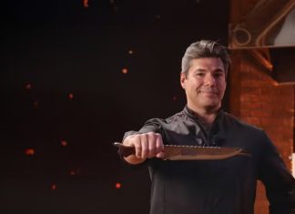 ‘No Fogo com Bronze’: Chefe de cozinha encara desafios na churrasqueira em novo reality show Chef in black uniform extending a large knife toward the camera in a studio kitchen backdrop with brick walls and warm lighting.