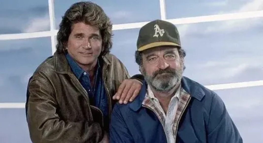 Two men in casual jackets posing together, one with a brown leather jacket and the other wearing a cap, hand on the other's shoulder.