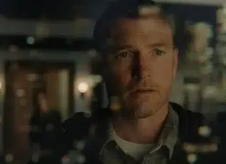 Close-up of a man with a pensive expression, looking slightly to the side, with blurred city lights reflected on glass surrounding him