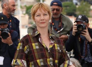 Woman in a plaid shirt stands at the center, posing as photographers surround her at an outdoor media event.