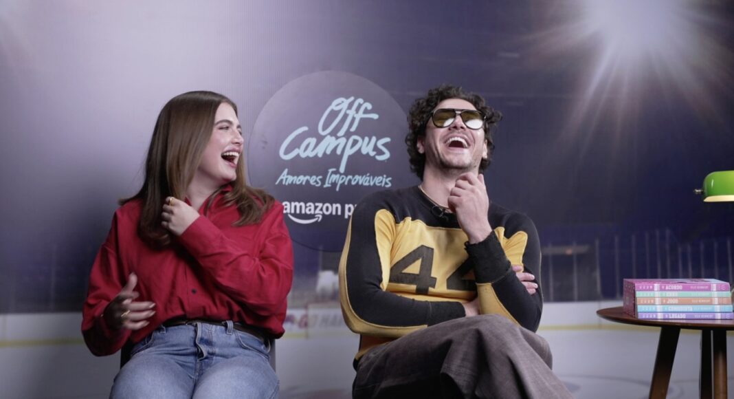 Screenshot 2026-05-14 at 8.53.11 PM Two friends sit and laugh on a set, with an 'Off Campus' logo in the background; woman in red shirt, man in a yellow-and-black sweater sits to her right, wearing sunglasses.