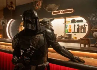 Mandalorian in black armor at a bar with Grogu perched on his shoulder, dim sci‑fi tavern setting.