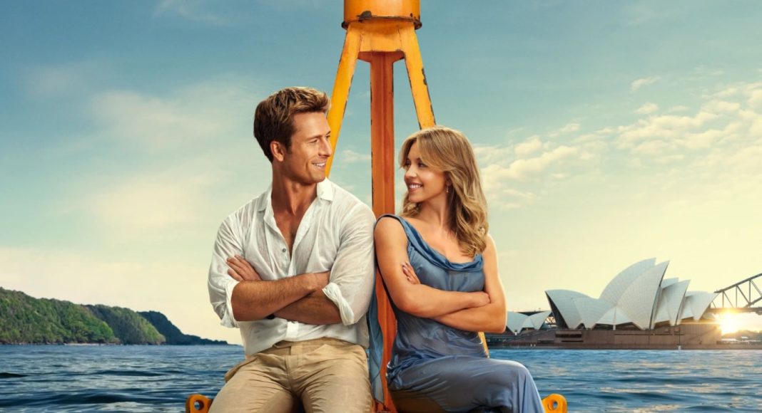 Couple sitting back-to-back on a yellow boat frame, arms crossed, smiling at each other with Sydney Opera House in the background.