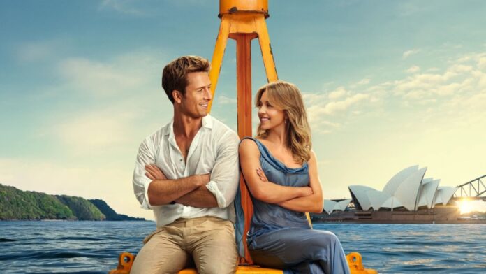 Couple sitting back-to-back on a yellow boat frame, arms crossed, smiling at each other with Sydney Opera House in the background.