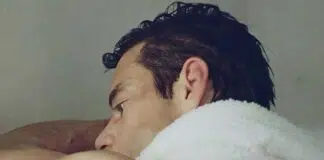 Close-up side profile of a man resting his head on a white towel over his shoulder.