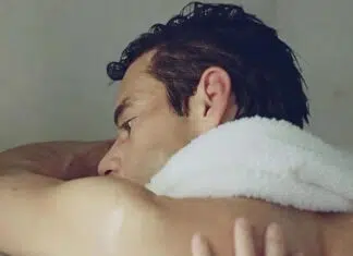 Close-up side profile of a man resting his head on a white towel over his shoulder.