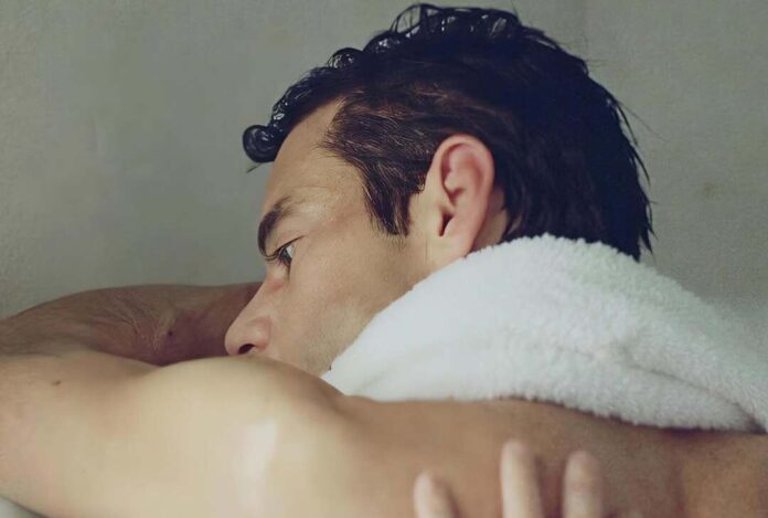 Close-up side profile of a man resting his head on a white towel over his shoulder.