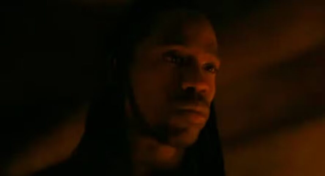 Hooded man in low, orange light with a contemplative expression (close-up)