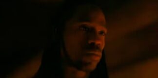 Hooded man in low, orange light with a contemplative expression (close-up)