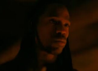Hooded man in low, orange light with a contemplative expression (close-up)