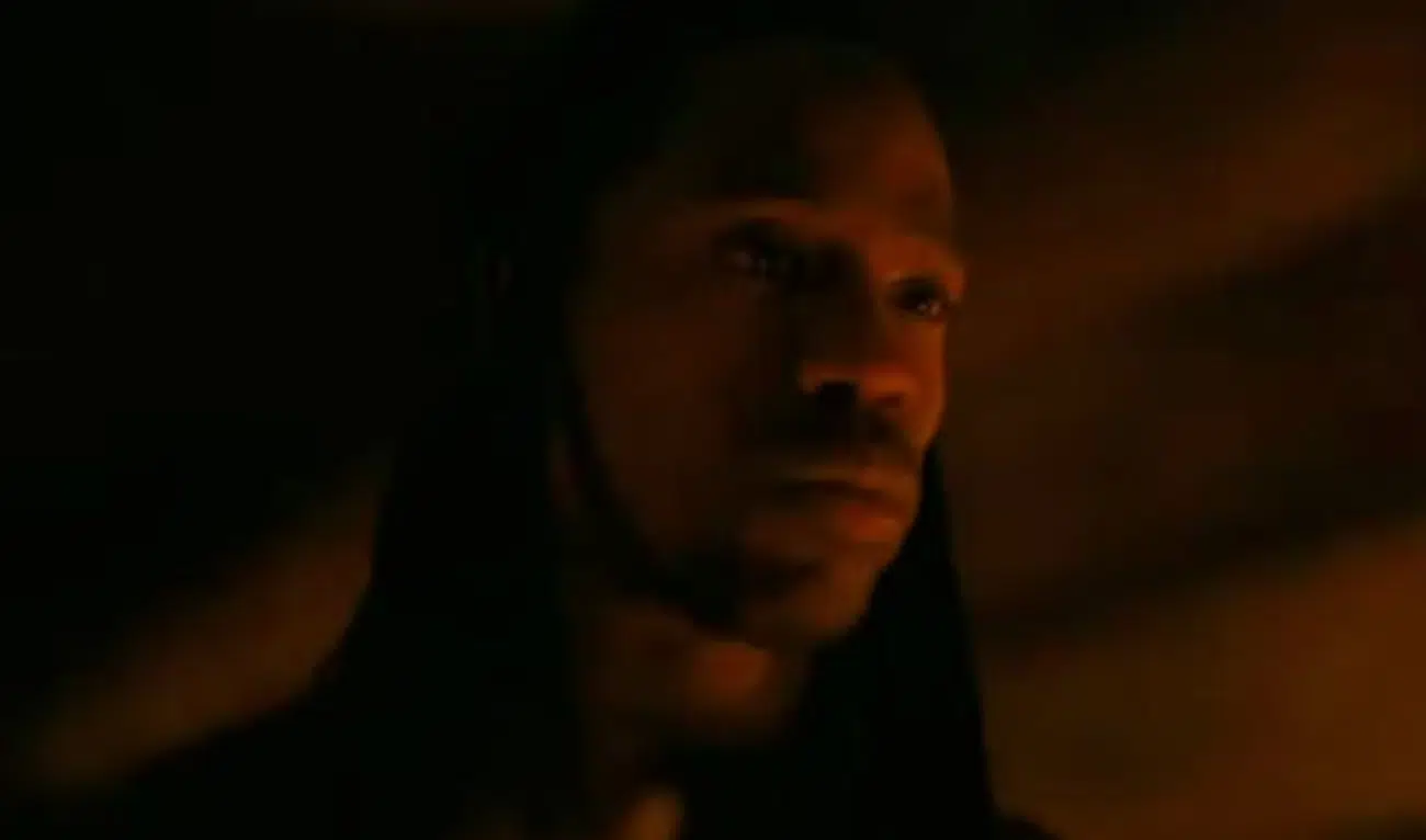 Hooded man in low, orange light with a contemplative expression (close-up)