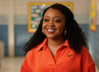 Smiling woman with curly hair wearing an orange polo in a school hallway? portrait in a soft focus setting.