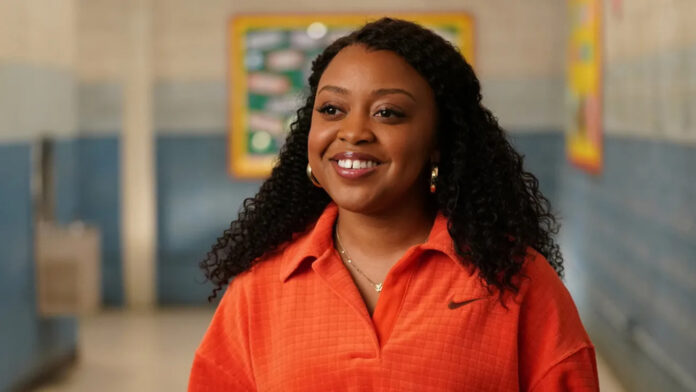 Smiling woman with curly hair wearing an orange polo in a school hallway? portrait in a soft focus setting.