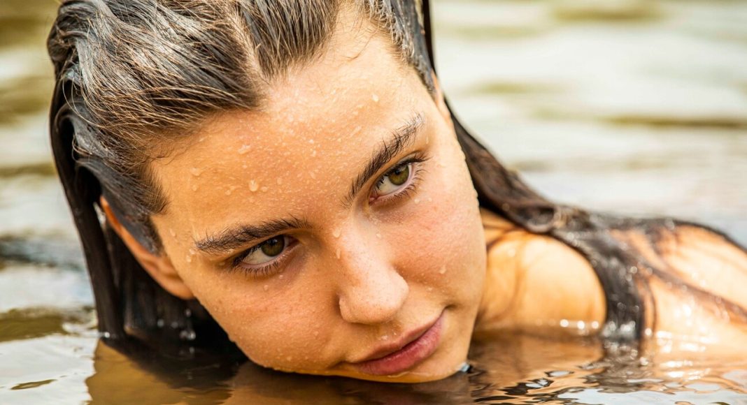alanis-guillen-pantanal (1) Close-up of a woman with wet hair resting her chin on water, gazing to the side in outdoor water.