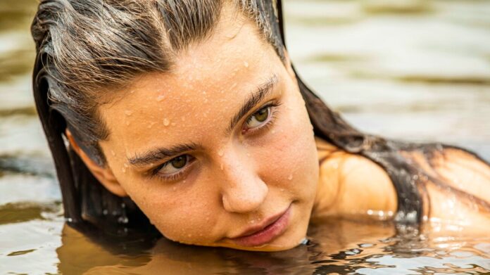 Close-up of a woman with wet hair resting her chin on water, gazing to the side in outdoor water.
