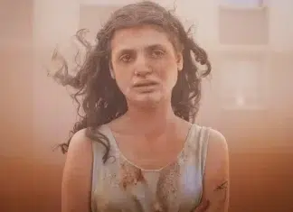Woman with curly hair, dirt-stained tank top, standing in a dusty, hazy environment.