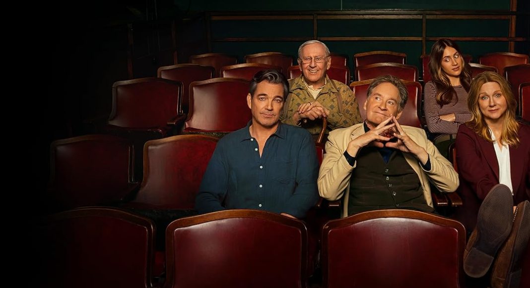 Six people sit in a theater row of red seats, smiling at the camera.