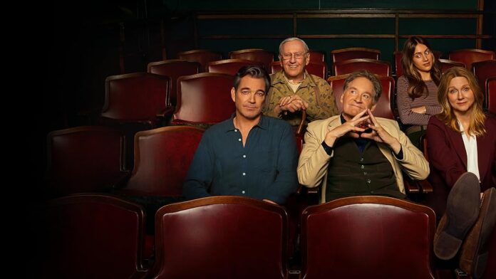 Six people sit in a theater row of red seats, smiling at the camera.