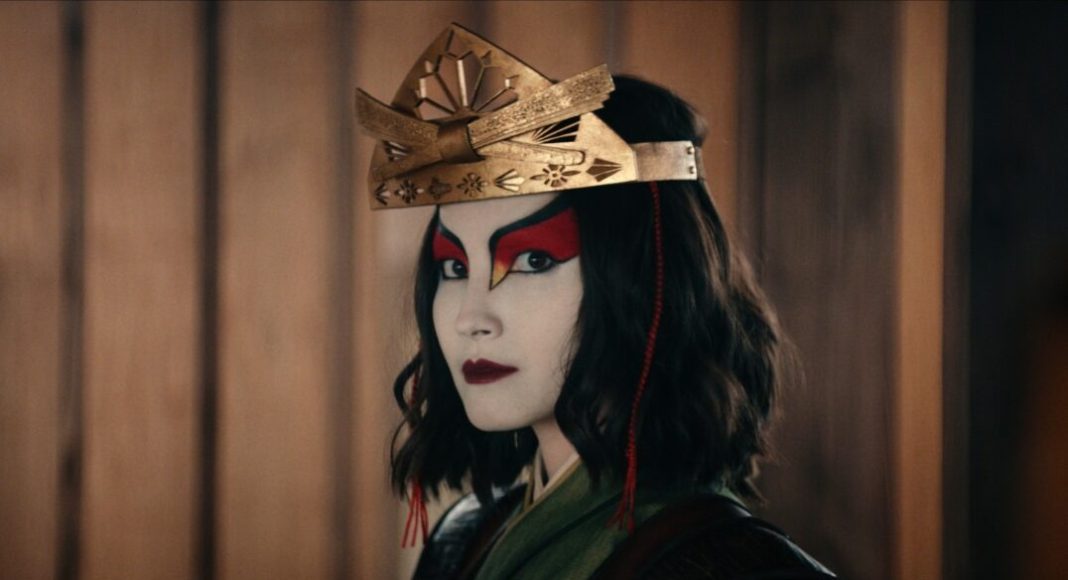 Cosplayer with pale makeup and bold red eye accents, wearing a decorative gold crown, facing the camera.