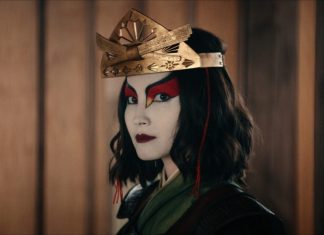 Cosplayer with pale makeup and bold red eye accents, wearing a decorative gold crown, facing the camera.