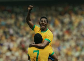 Two Brazilian soccer players celebrate a goal, one lifts a fist in the air as the other carries him on his shoulders in a crowded stadium