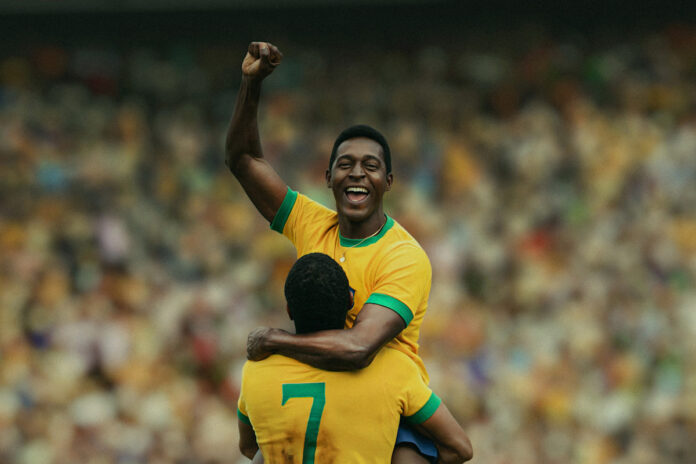 Two Brazilian soccer players celebrate a goal, one lifts a fist in the air as the other carries him on his shoulders in a crowded stadium
