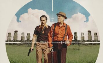 Two men stand side by side in a field, seen through a crosshair scope, one holding a pistol and the other a briefcase.