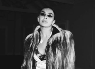 Portrait of a woman wearing a long fur coat, with bold smoky makeup, looking slightly upward at the camera in a monochrome fashion shot.