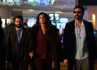Three stylish adults walk through a bright casino lobby; a woman in a burgundy suit and fur coat leads, flanked by two men in suits.