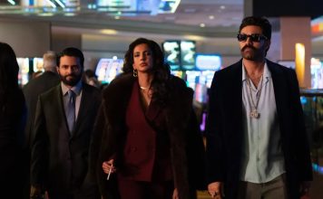 Three stylish adults walk through a bright casino lobby; a woman in a burgundy suit and fur coat leads, flanked by two men in suits.