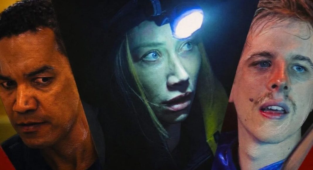 Three close-up faces in dramatic lighting: a man on the left, a woman with a headlamp in the center, and a man on the right, all looking in different directions.