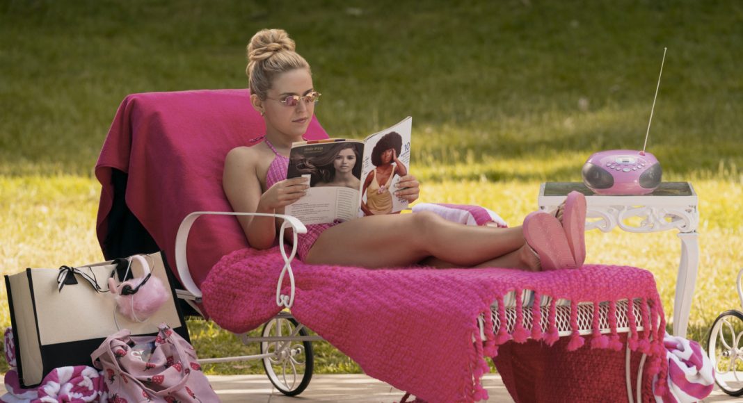 Woman sunbathing on a pink chaise lounge outdoors, reading a magazine with a pink throw, surrounded by pink accessories and a pink mini radio.