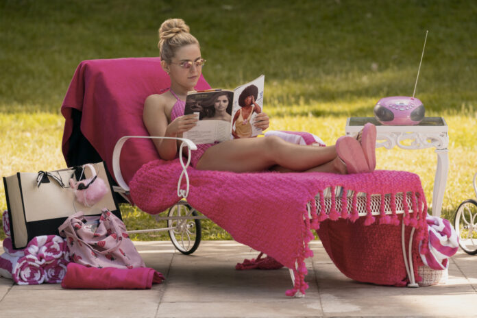 Woman sunbathing on a pink chaise lounge outdoors, reading a magazine with a pink throw, surrounded by pink accessories and a pink mini radio.