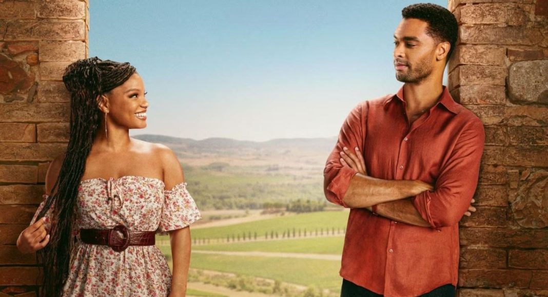 eu e você na toscana Woman in a floral off-shoulder dress with a belt smiles at a man in a red shirt as they stand between stone pillars with a rural landscape behind them.