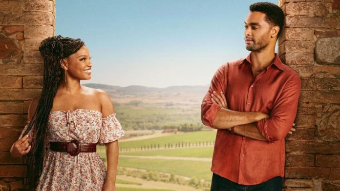Woman in a floral off-shoulder dress with a belt smiles at a man in a red shirt as they stand between stone pillars with a rural landscape behind them.