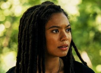 Portrait of a woman with long black dreadlocks looking to the right, outdoors with green foliage in the background.