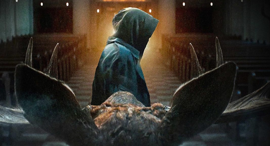 geracao Hooded figure in a cloak stands at the end of a church aisle, viewed from behind, with a large animal skull in the foreground.
