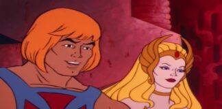 He-Man with orange hair and blue armor stands beside She-Ra in a pink, cavern-like setting, smiling.